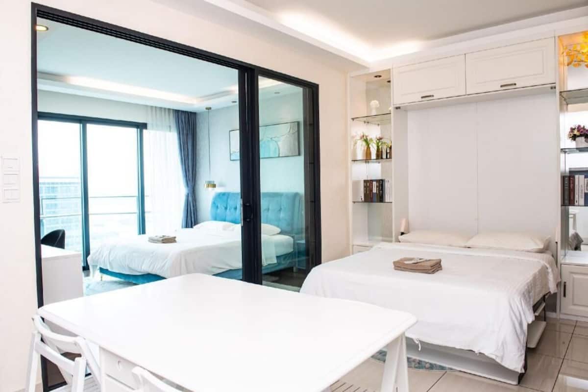 Quarto de hotel com duas camas, uma escrivaninha e uma porta de vidro deslizante que dá para uma varanda.