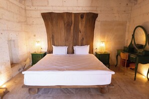 Een bed met een houten hoofdbord, twee nachtkastjes met lampen, een stoel en een spiegel op een groene dressoir.