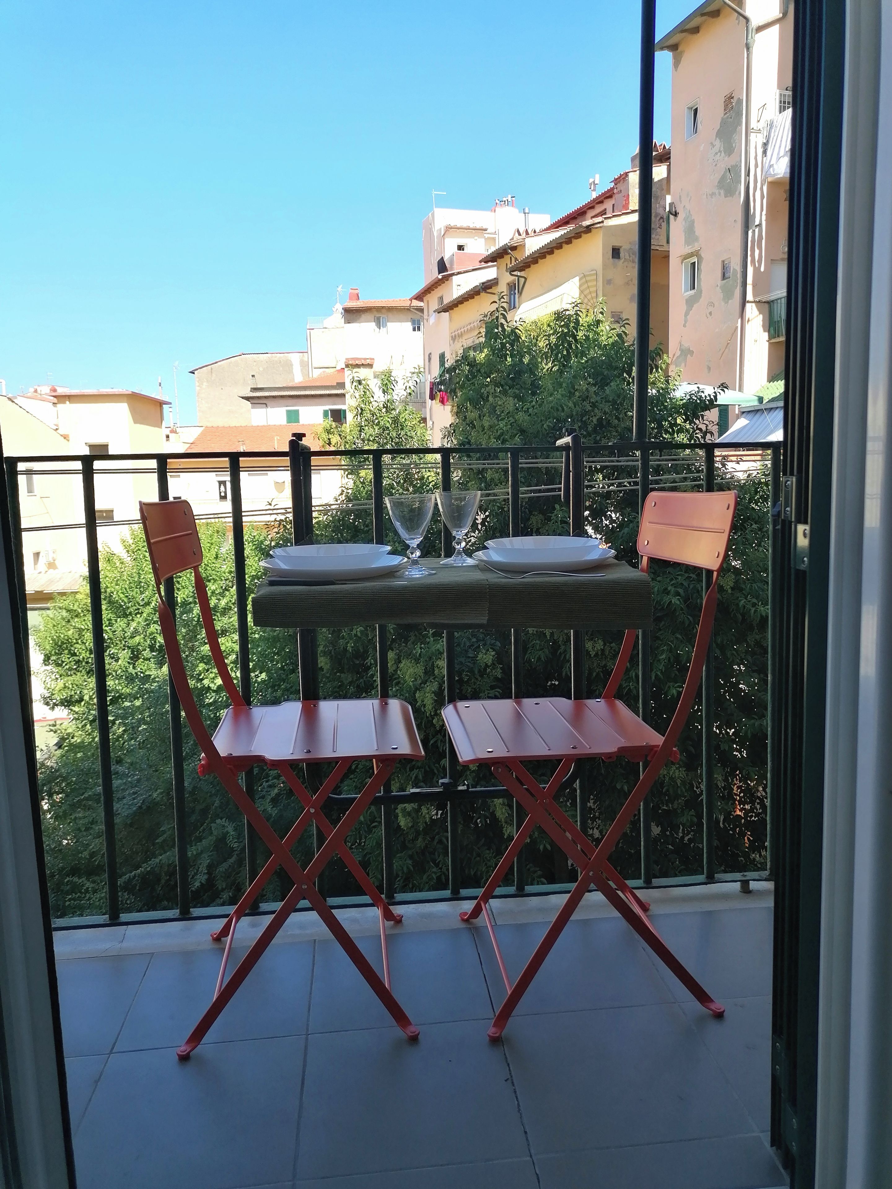Een balkon met een tafel en twee stoelen, met uitzicht op een woongebied met gebouwen en bomen.