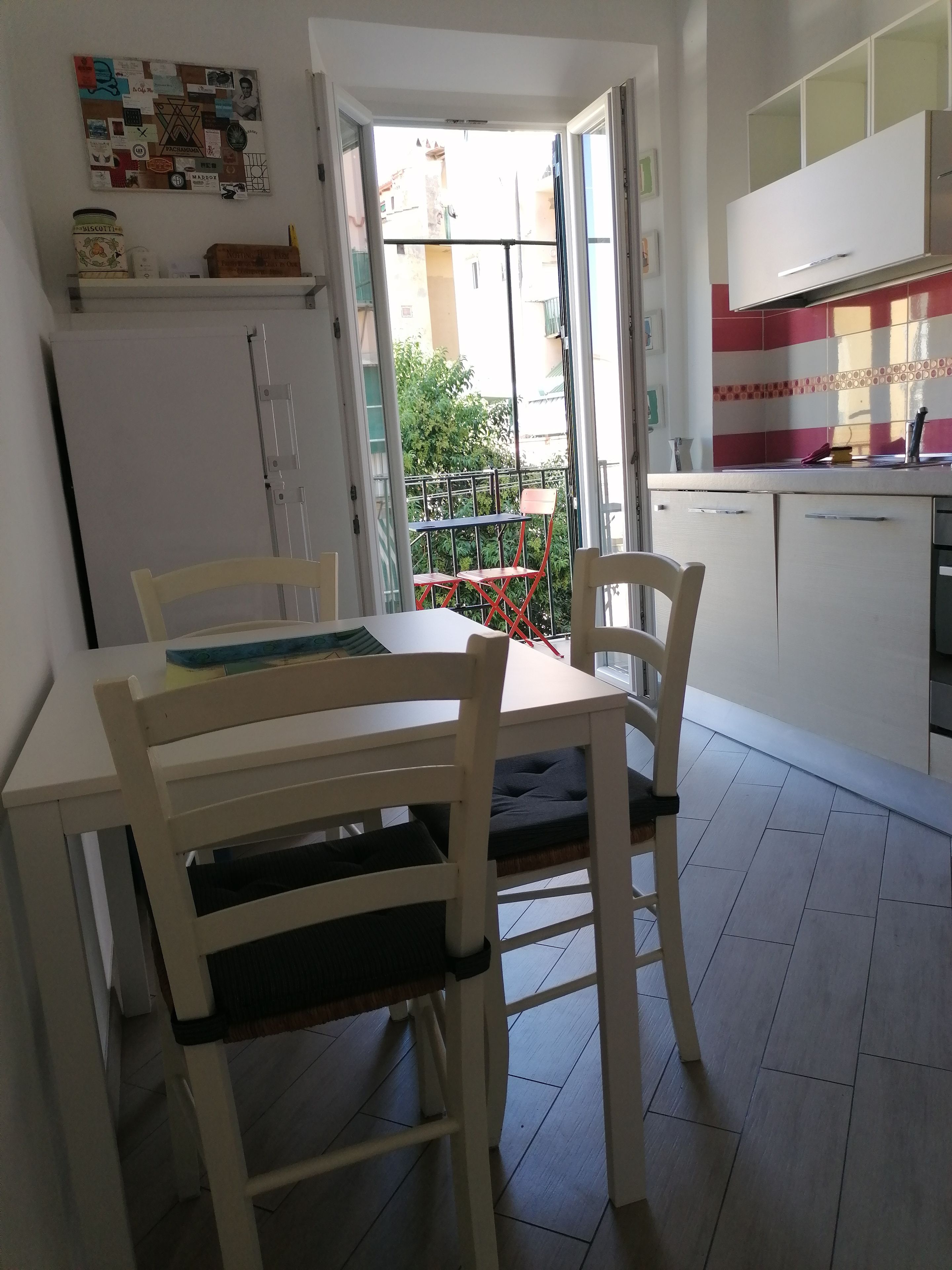 Een keuken met een eettafel en stoelen, een koelkast en uitzicht op buiten.
