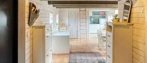 A narrow hallway with a kitchen area on one side, featuring cabinets, a refrigerator, and a small table with a plant.