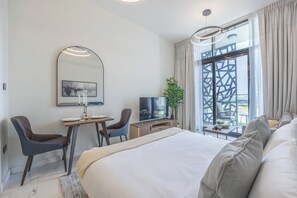 A modern hotel room with a large bed, a desk with two chairs, a television, and a large window with curtains. - Bloomfields Studio in The Gate - Masdar (Abu Dhabi)