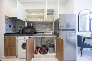 A compact kitchen with a washing machine, a microwave, and a refrigerator. - Bloomfields Studio in The Gate - Masdar (Abu Dhabi)