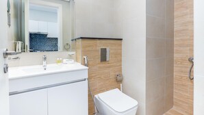 A modern bathroom with a white sink, mirror, and toilet. - Bloomfields Vibrant Stu in The Gate (Abu Dhabi)