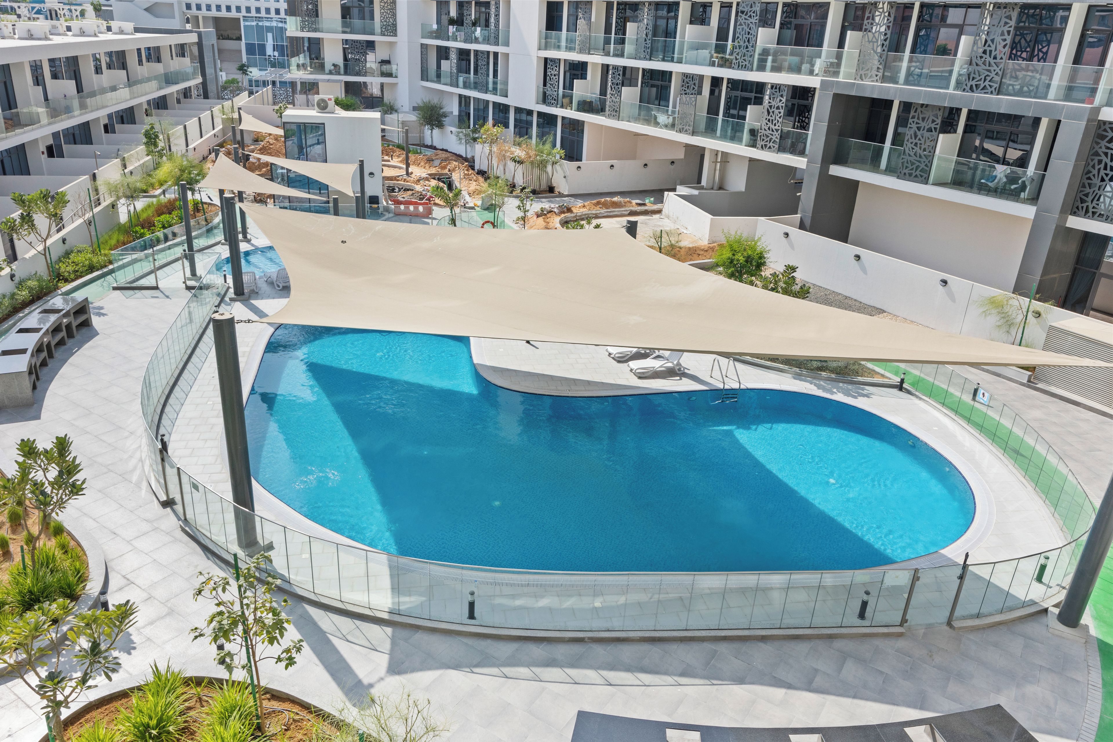 A modern outdoor swimming pool with a glass enclosure, surrounded by a landscaped area with plants and seating.