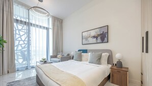 A modern bedroom with a large bed, a side table, a nightstand, a lamp, and a painting on the wall. - Bloomfields Vibrant Stu in The Gate (Abu Dhabi)