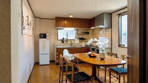 A compact kitchen with a dining area, wooden cabinets, a refrigerator, and a window providing natural light. - 福助Hakuro   double bath; 5mins to Metro;Nipponbashi Namba7mins;Nara direct (大阪市 東成区　大今里西 3-13-10)