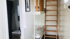 En smal gang med en køjeseng, en træstige og en hængende lampe.