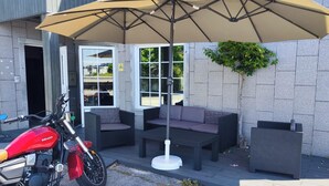 A motorcycle parked outside a building with a patio area featuring a table and chairs, and a large umbrella providing shade.
