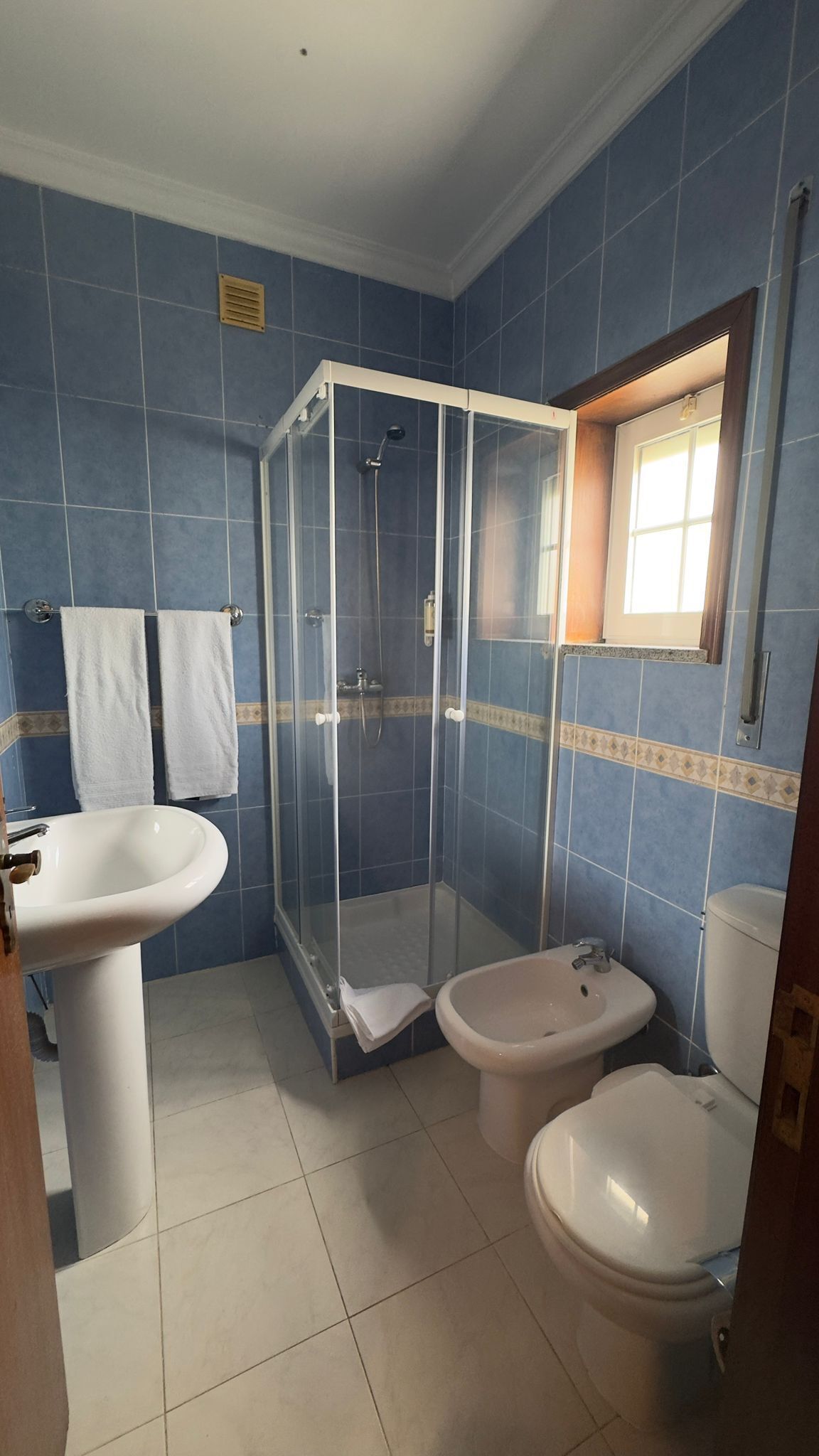 Un baño con ducha de vidrio, dos lavamanos, un bidé y un inodoro.