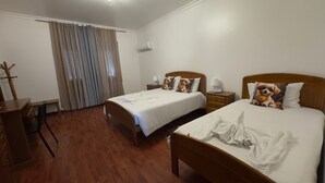 A hotel room with two beds, a desk, a chair, a wardrobe, and a window with curtains.