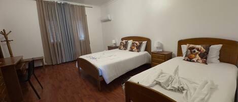A hotel room with two beds, a desk, a chair, a wardrobe, and a window with curtains.