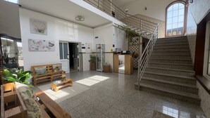 A spacious lobby with a staircase, a reception desk, and a seating area with a bench and table.