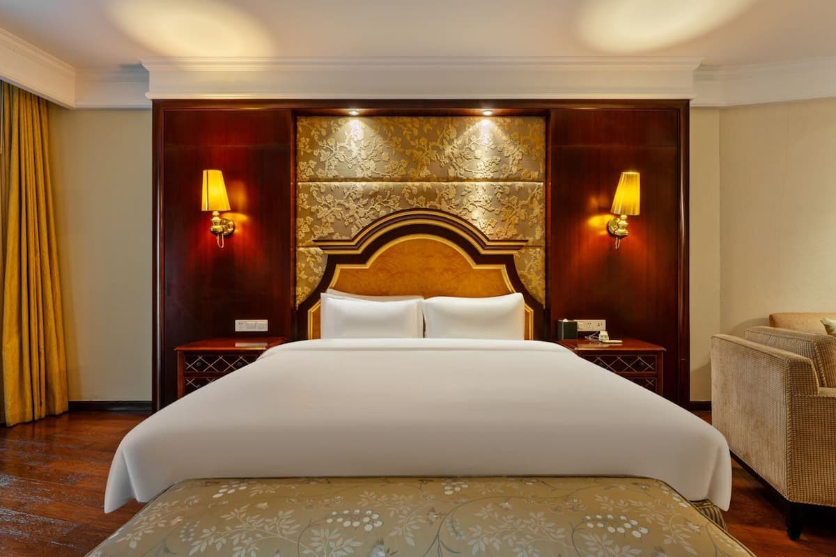 Una habitación de hotel con una cama grande, dos mesitas de noche, una silla y un cabecero decorativo.