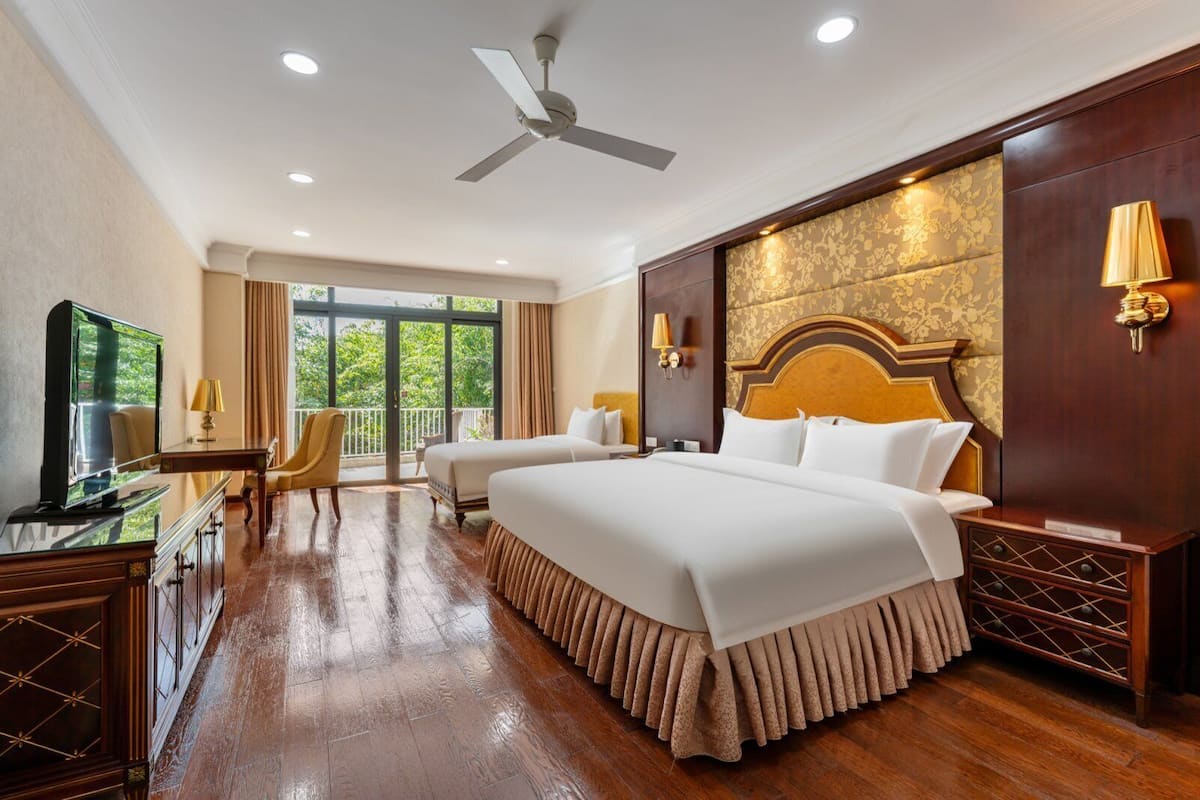 Habitación de hotel con dos camas, televisión, escritorio y balcón con vistas.