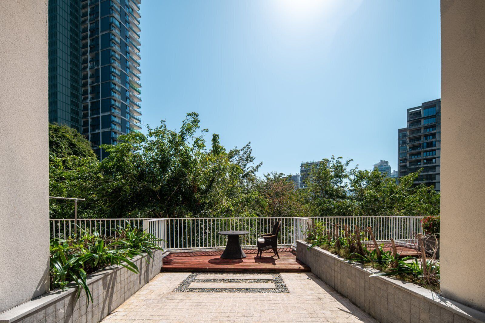 Una terraza en la azotea con una mesa y sillas, rodeada de vegetación y edificios altos.