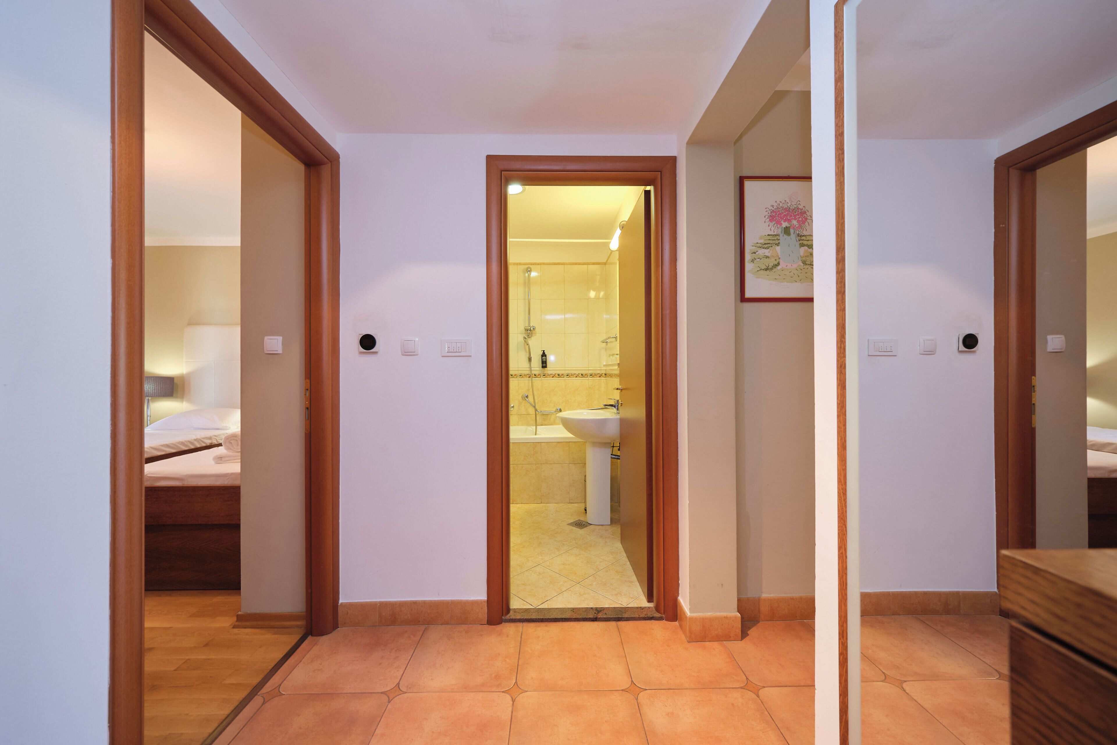 Une chambre d’hôtel avec une porte en bois, un lit, une salle de bain avec un lavabo et un sol carrelé.