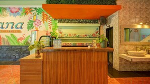 Un espace d’accueil doté d’un comptoir en bois, d’une fresque murale représentant des plantes tropicales et d’un sol carrelé.