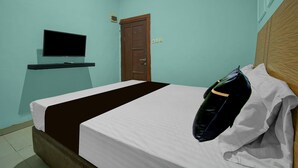Un lit simple avec une couvre-lit blanche et marron, un téléviseur fixé au mur et une porte en bois.