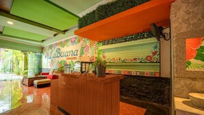 Un espace d’accueil avec un bureau en bois, une enseigne « LaBuana » et une fresque murale aux motifs floraux.