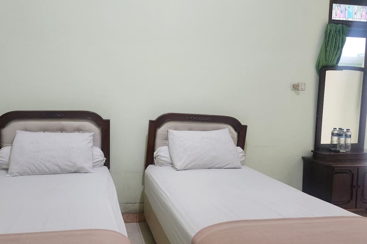 Deux lits simples avec des têtes de lit en bois, du linge de lit blanc et une petite armoire en bois contenant des bouteilles.