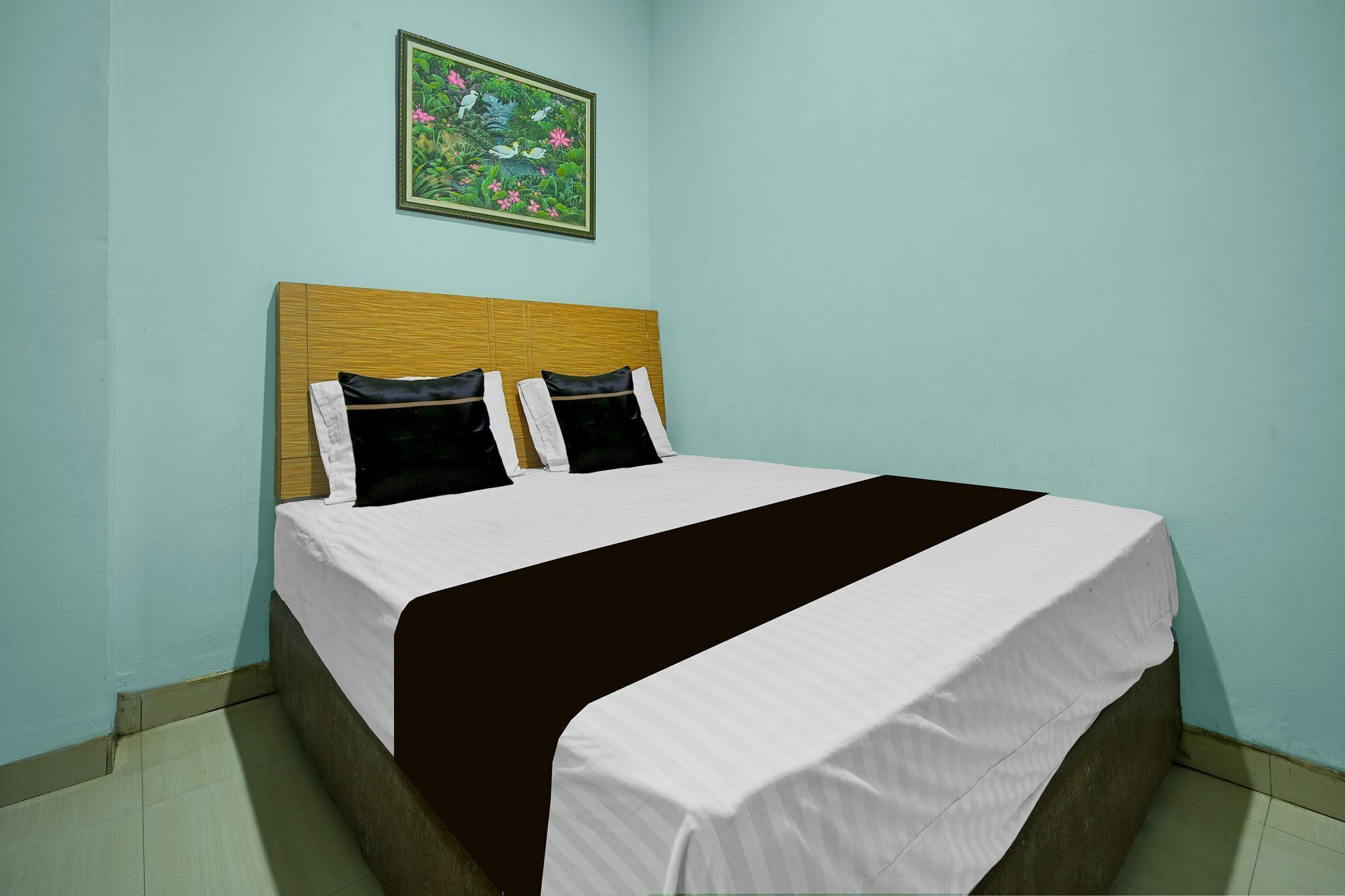 Een net opgemaakt bed met een bruin-witte deken, twee kussens en een hoofdbord tegen een lichtblauwe muur.