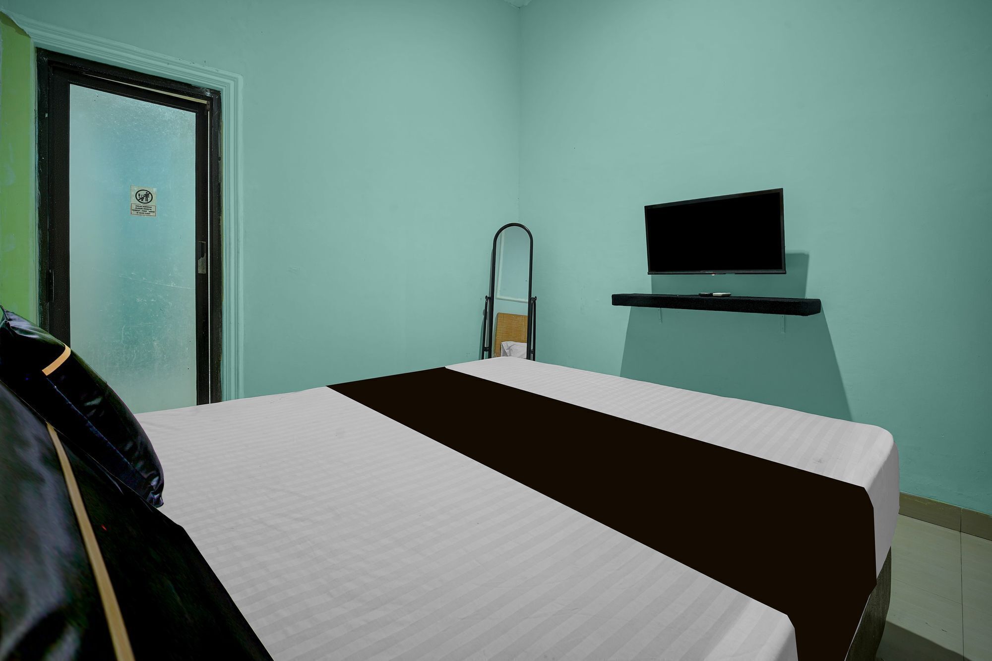 A single bed with a white and brown bedspread in a room with teal walls, a television on a black stand, and a door with a sign.