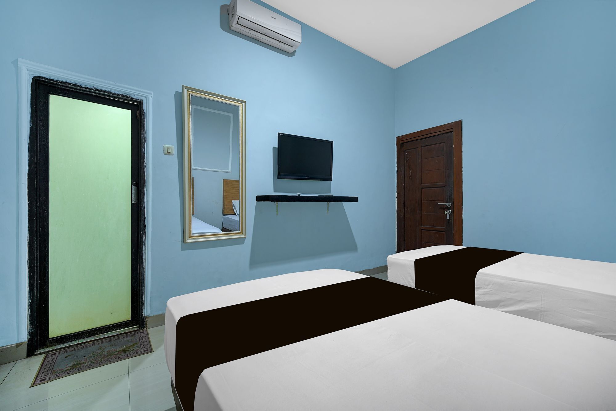 A hotel room with two beds, a television, a mirror, and an air conditioning unit.