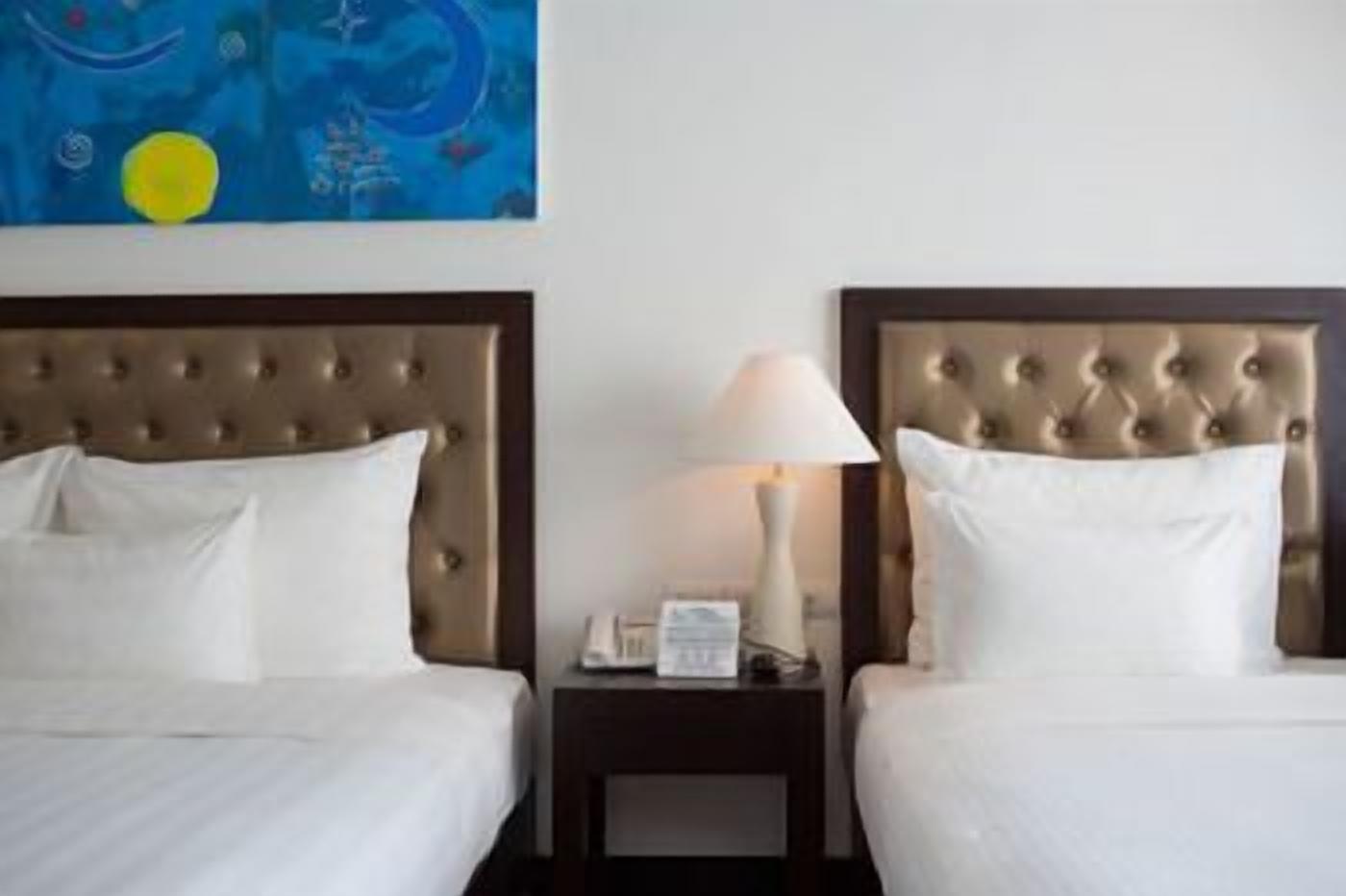 A hotel room with two beds, a nightstand with a lamp, and a painting on the wall.
