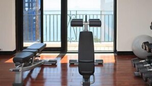 Een sportschool met trainingsapparatuur, grote ramen en uitzicht op gebouwen.
