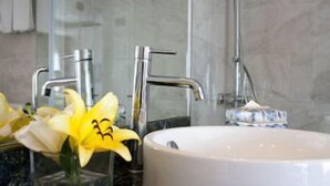 Een badkamer met een wit wastafel, een glazen vaas met gele bloemen, en een zakdoekendoos.