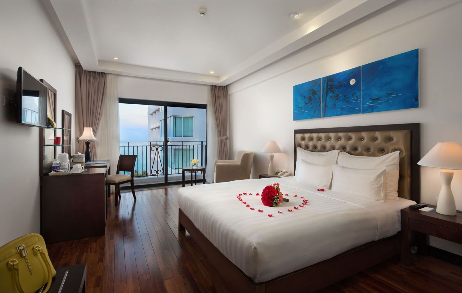 A hotel room with a large bed, a balcony, a desk with a chair, and a TV.