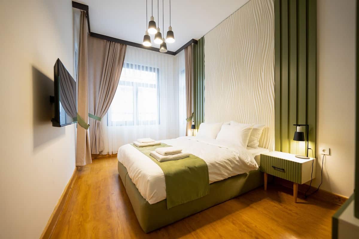 A modern bedroom with a bed, bedside table, lamp, and a TV mounted on the wall.