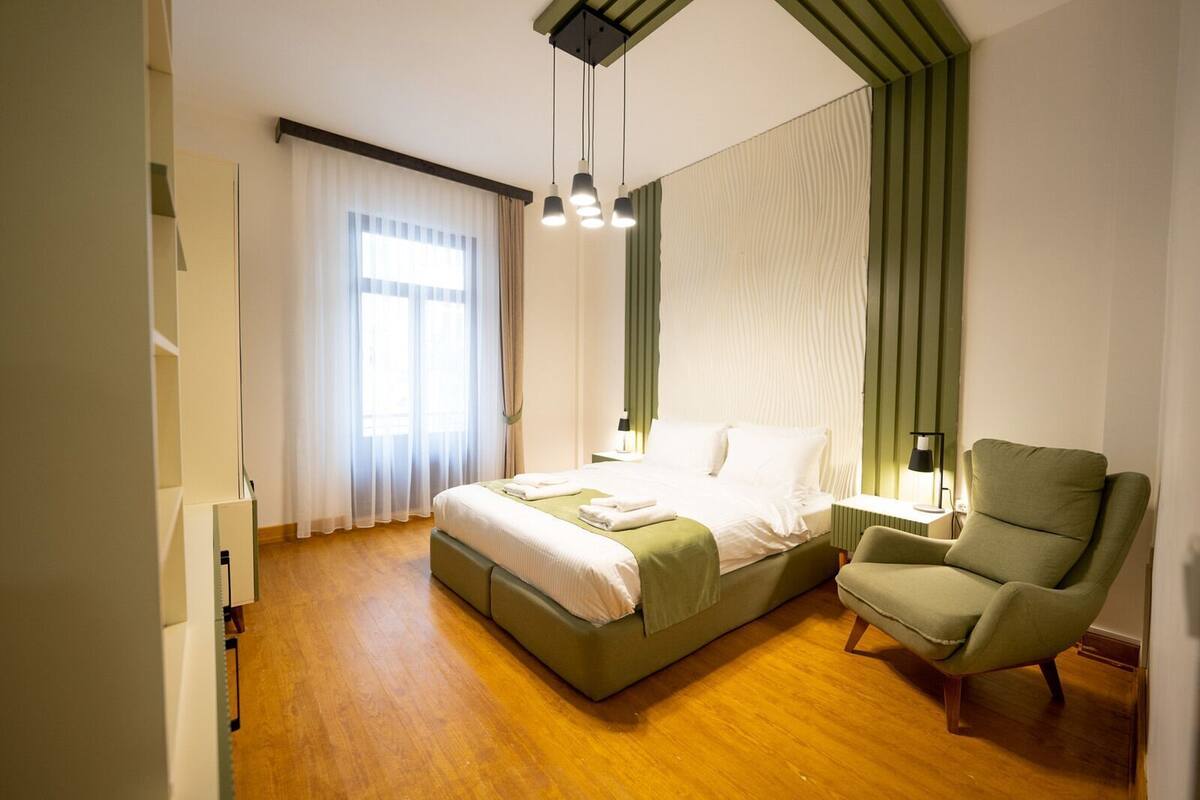 A bedroom with a bed, a chair, a nightstand, and a window with curtains.