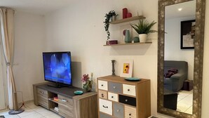 A living room with a flat-screen TV, a wooden cabinet with drawers, a mirror, and a sofa.