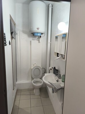 Un baño pequeño y limpio con inodoro, lavamanos y calentador de agua.