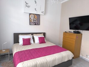 Un dormitorio con cama, televisor, cómoda y decoración en la pared.