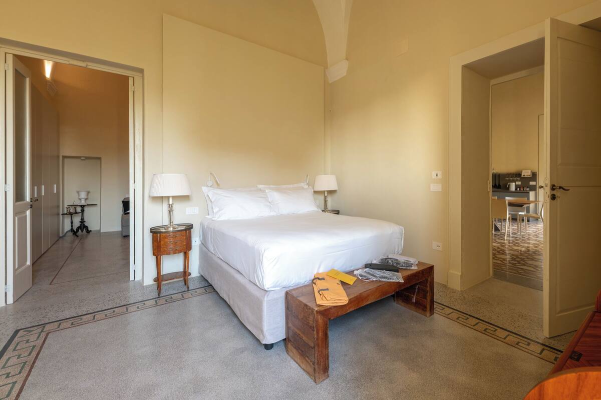 Habitación de hotel con cama, mesitas de noche, lámpara y una pequeña mesa con objetos encima.