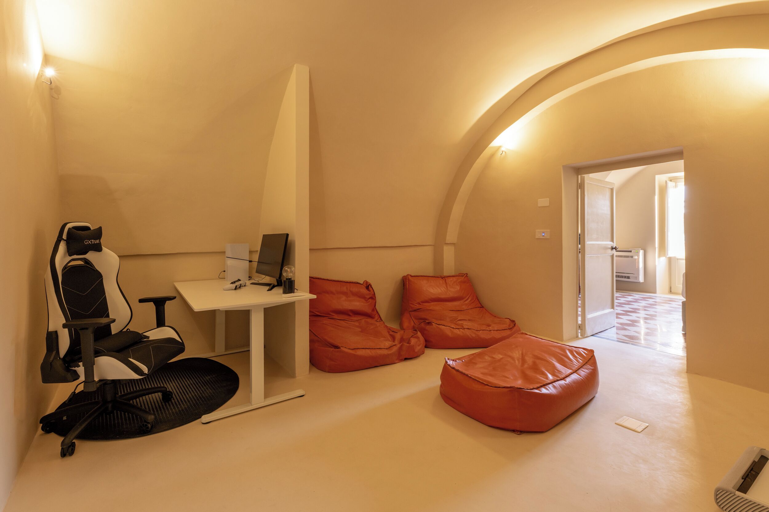 A modern room with a white desk, a gaming chair, and two orange bean bags.
