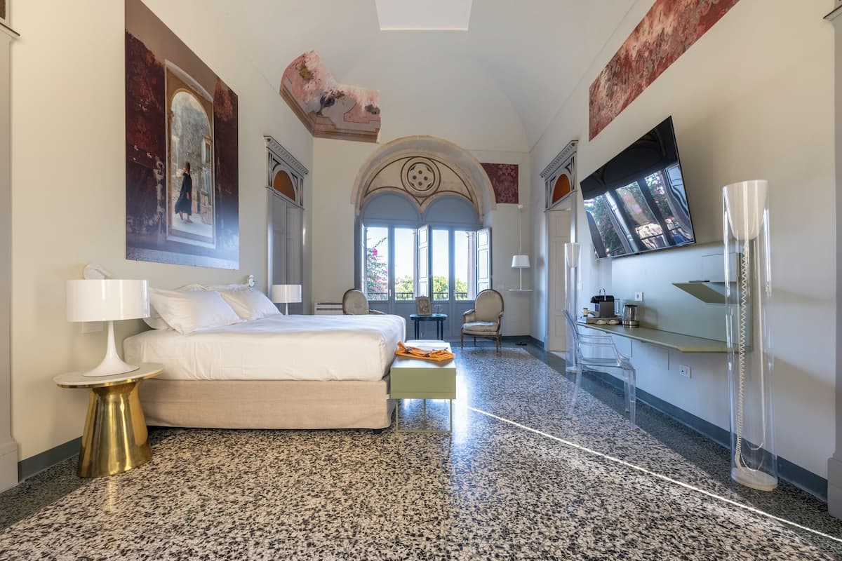 Una habitación de hotel con una cama, un escritorio, una silla, un televisor y un ventanal grande.