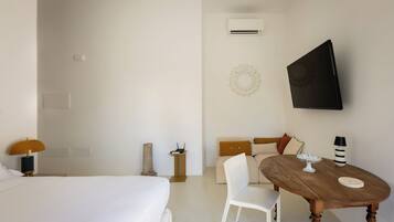 Une chambre d’hôtel avec un lit, une petite table avec une lampe, un canapé et un téléviseur fixé au mur.