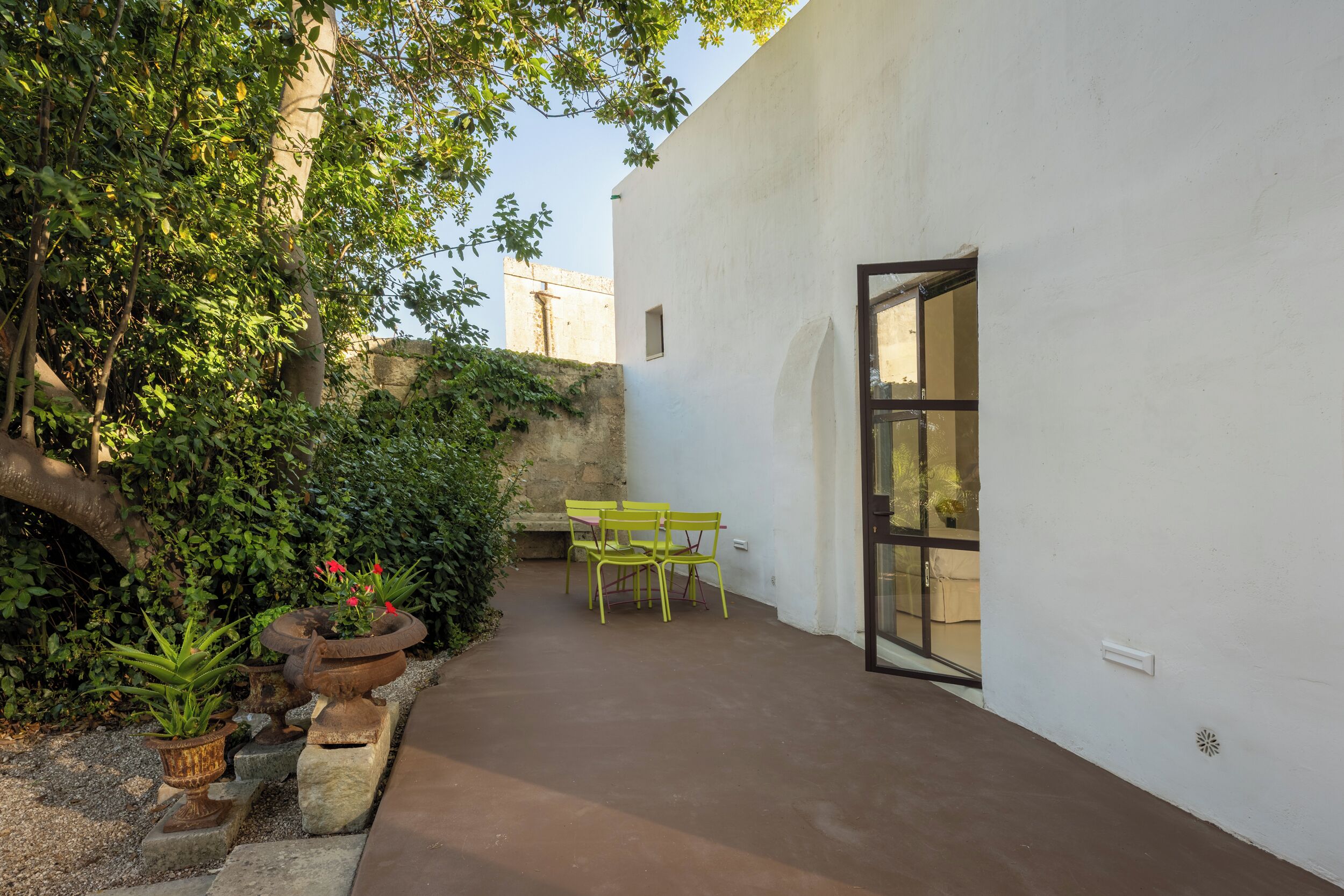 Un cortile con un muro bianco, un tavolo con sedie e piante in vaso.