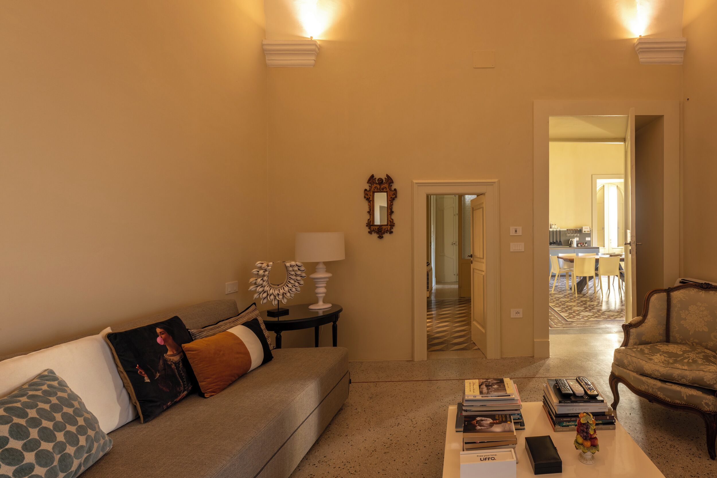 Een woonkamer met een bank, salontafel en fauteuils. Er is een deur die naar een andere kamer leidt.