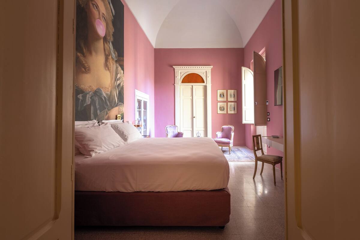Un dormitorio con una cama grande, una silla, un escritorio y una puerta que da a otra habitación.