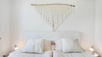 Een slaapkamer met een bed, twee bedlampen en een macramé wanddecoratie.
