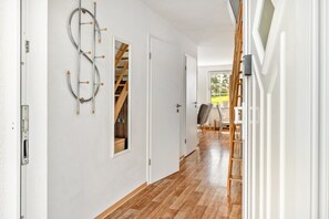 Un pasillo con suelo de madera, paredes blancas, una escalera a la vista y una puerta que da a otra habitación.