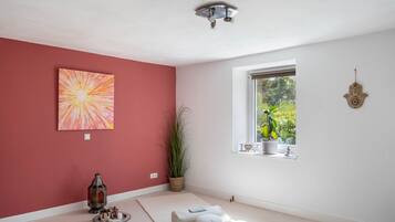 A room with a red wall, a large abstract painting, a window with a view of greenery, and a ceiling light fixture.