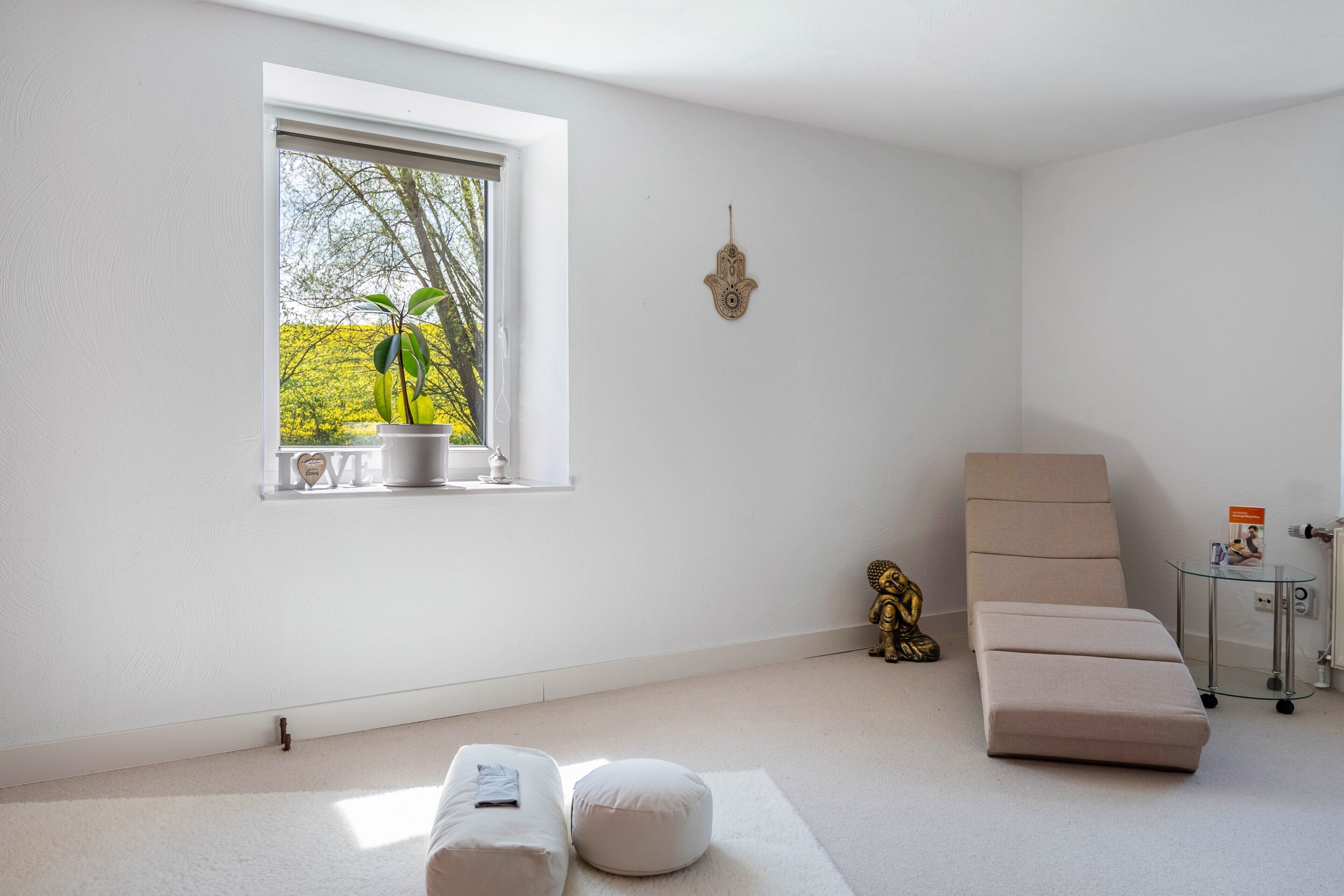 A minimalist room with a window, a potted plant, a Buddha statue, a sofa, and a small table.