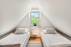 A small, well-lit room with two single beds, a small table, a window with a view of greenery, and a sloped ceiling. - Sunset Vacation Apartment – Your Retreat in the Heart of Nature (Herzberg am Harz)