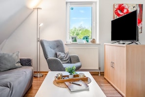 A cozy living room with a sofa, a chair, a coffee table with decorative items, a TV, and a cabinet. - Sunset Vacation Apartment – Your Retreat in the Heart of Nature (Herzberg am Harz)